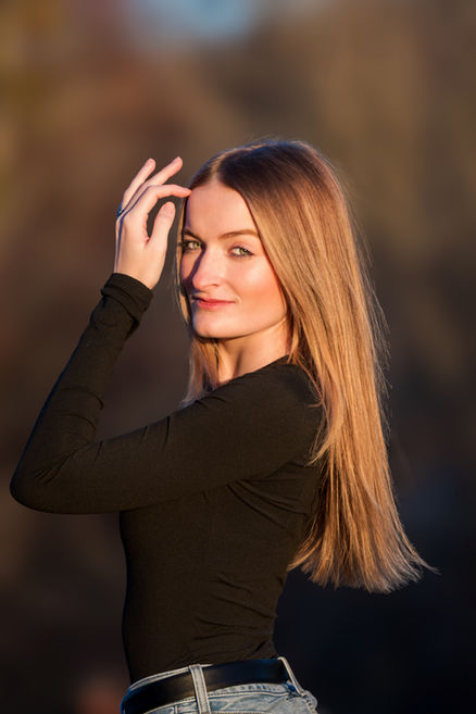 Portrait of a woman standing in a park with natural light, wind blowing through hair, personal branding photography.