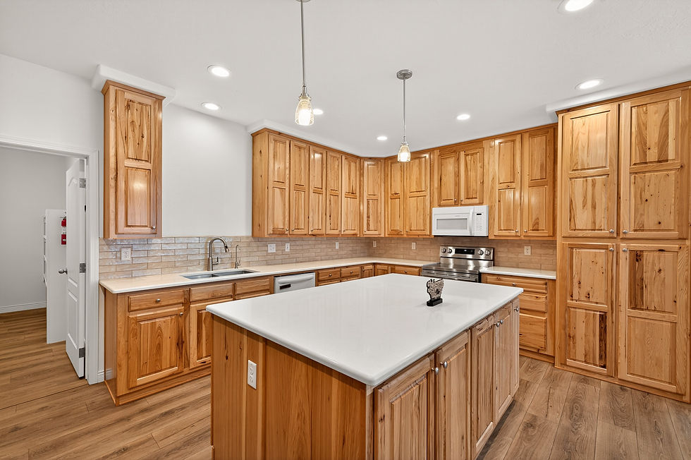 Bright modern kitchen with wood cabinets, white island, pendant lights, stainless appliances, and tan tile backsplash.