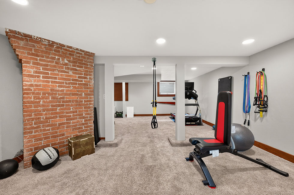 Basement home gym with treadmill, bench, resistance bands and exercise ball; brick accent wall and carpeted room.