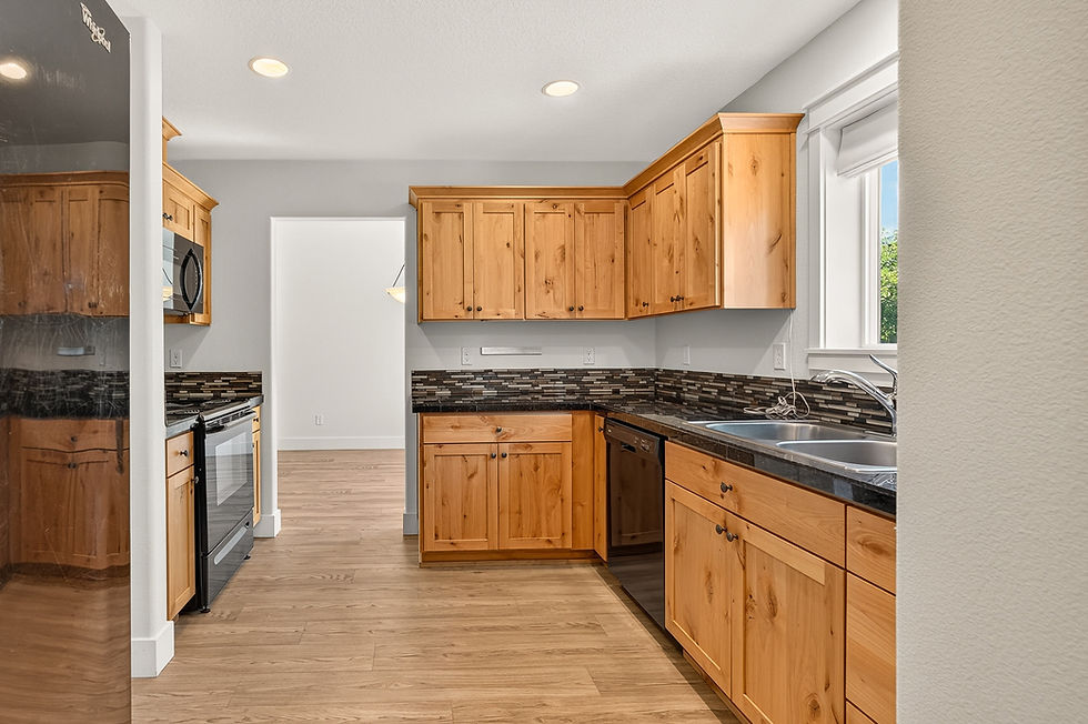Modern kitchen with honey wood cabinets, black countertops, stainless sink and stove, light wood floor, and a window.