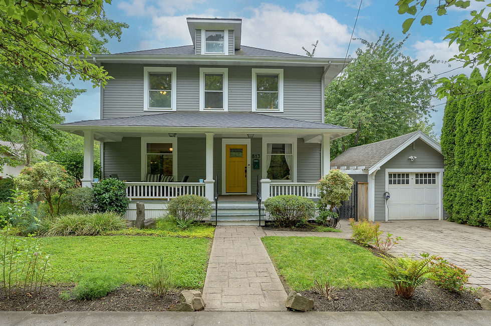 Gray two-story house with yellow front door, porch, and detached garage, framed by green trees and lawn.