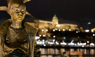 A statue at a tram stop in Budapest with Castle Hill by night in the background