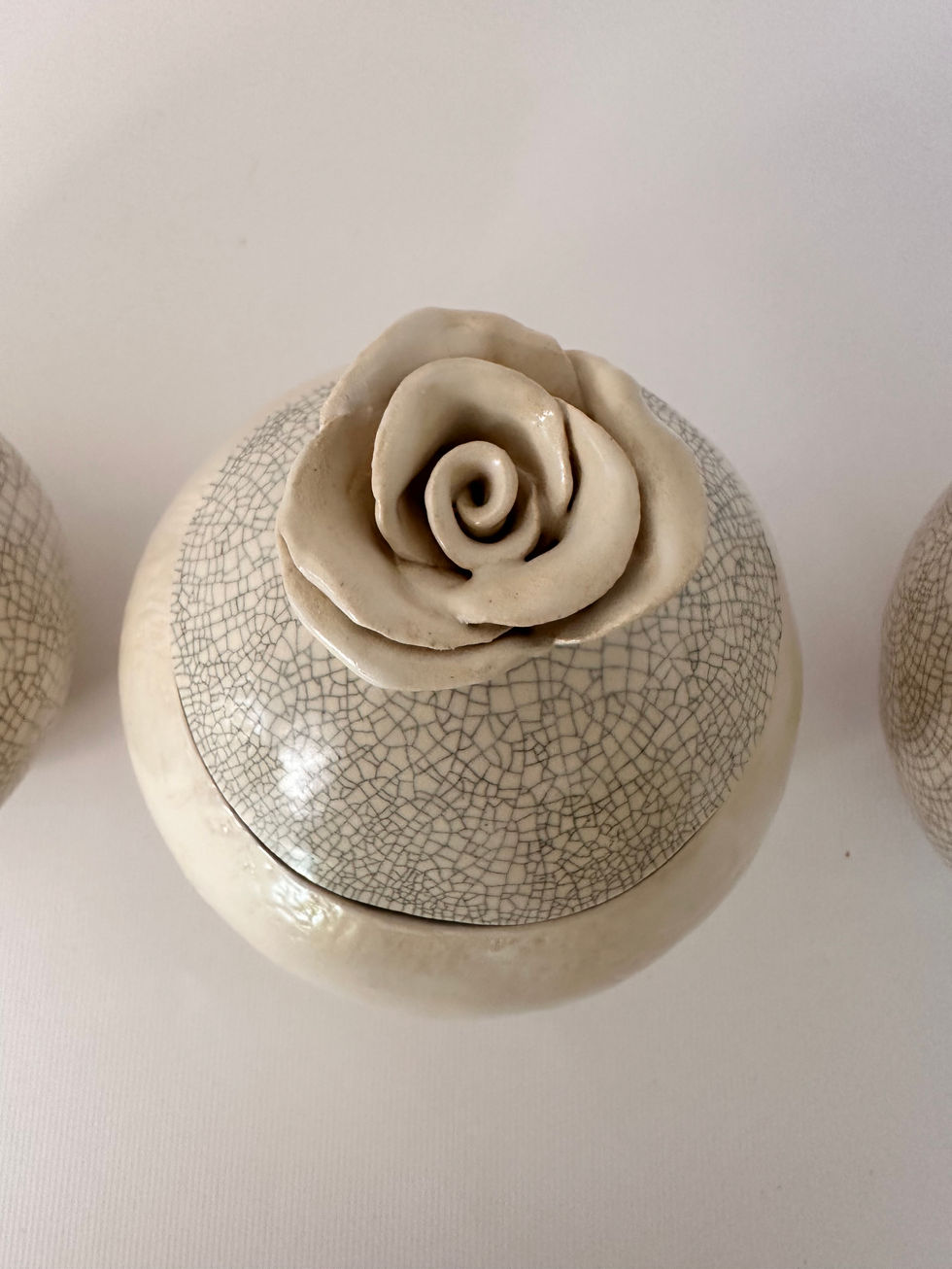 Een handgemaakte keramische urn met craquelé glazuur en een 3D roosje bovenaan, voor een deeltje van de assen en of een stukje stof van een kledingstuk van de overledene.