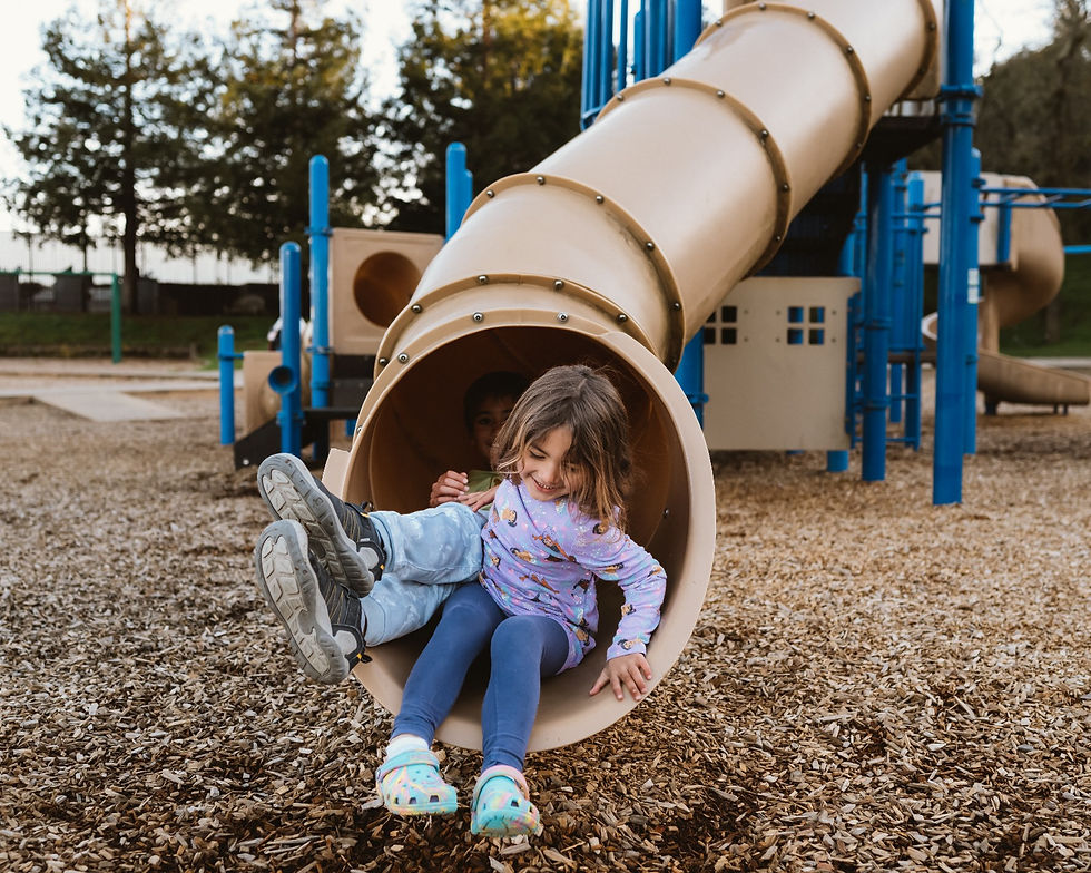 Two kids exiting from the same slide in a playground with wood chips on the ground