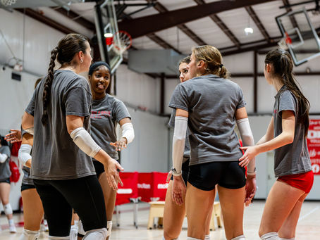 Volleyball players huddle for a team discussion during practice, showing camaraderie and focus on the court.