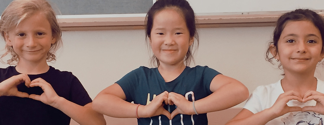 Three students sitting side by side smiling and forming heart shapes with their hands