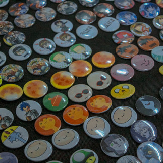 Imagem de diversos bottons com temas de desenhos animados e personagens de anime, distribuídos em uma superfície escura