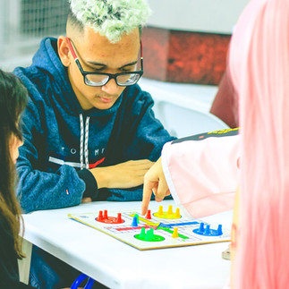 Jovem jogando jogo de tabuleiro com amigos em ambiente interno, focado na diversão e interação social