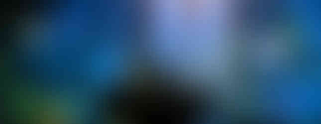 Orquestra ao vivo com maestro regendo uma apresentação com projeções coloridas no fundo