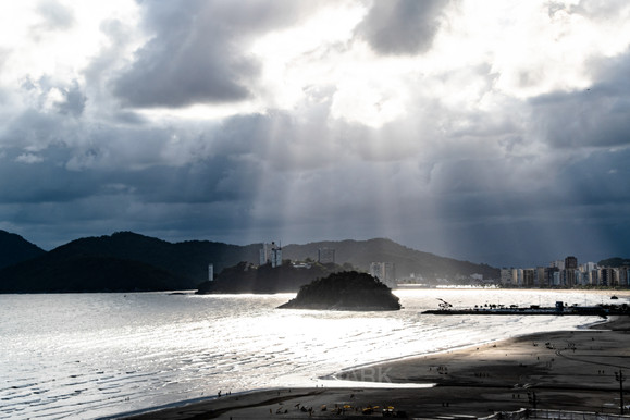 Sun rays shining through clouds on ocean and coastline with island.
