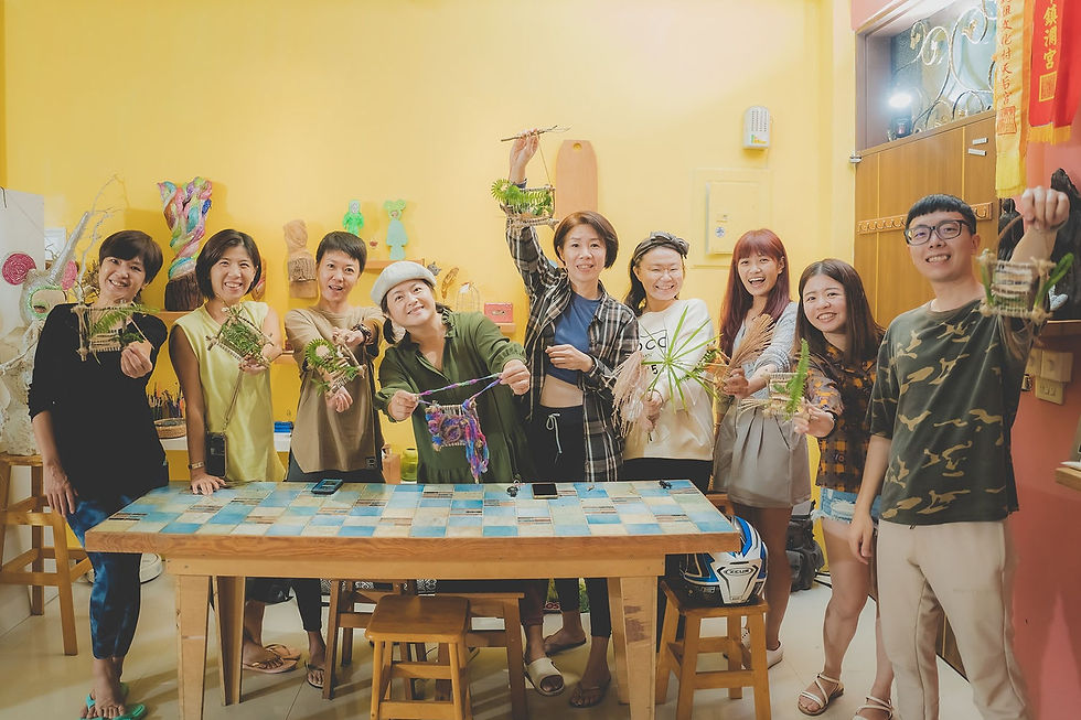 一群參與者在室內並排站立,手持由枝條、線繩與植物組成的手作作品。