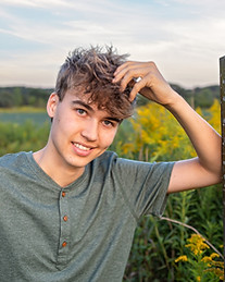 Handsome High School Senior boy leaning on a wooden post with his hand in his hair