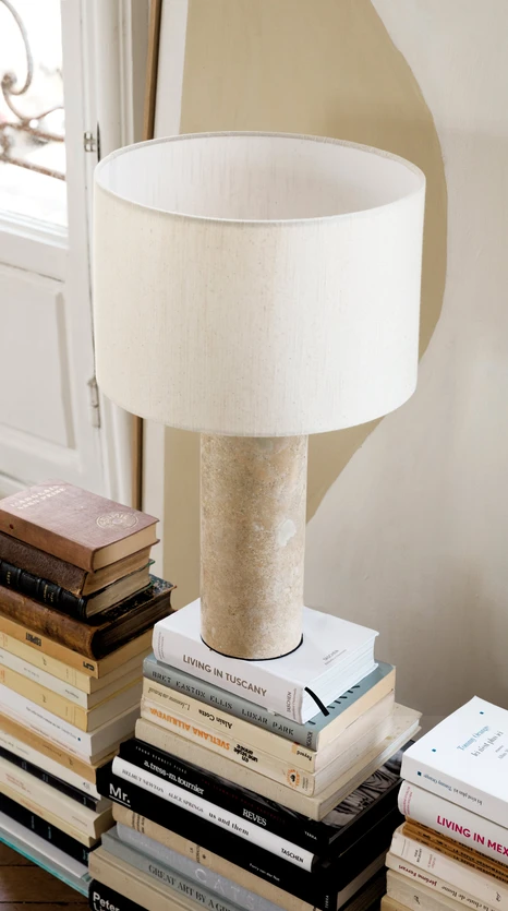 Lampe à poser NV Gallery en travertin beige, posée sur une pile de livres.