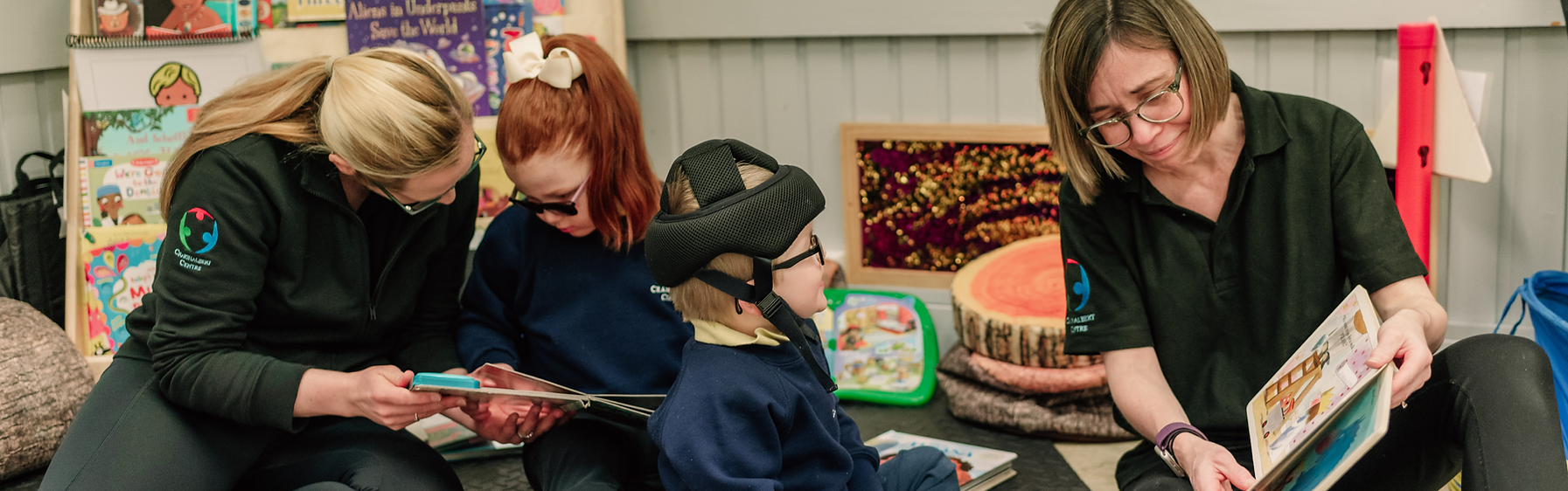 Two young children sitting on floor reading a book with staff.