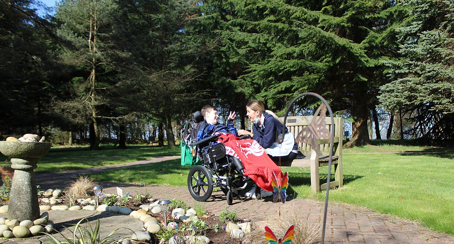 Young person enjoying the gardens at Craighalbert, staff member smiling at child as he shows his enjoyment.