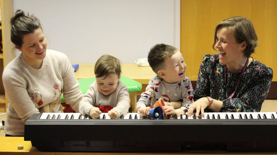 young boy and girl smiling as they play a keyboard with music therapist.