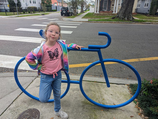 Girl in tie-dye hoodie next to blue bicycle sculpture