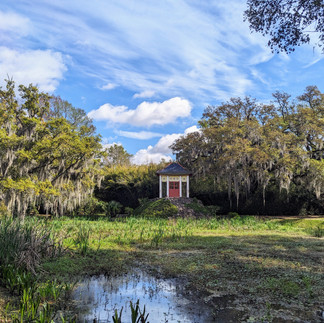 Gazebo with a red door by a pond and moss-draped trees