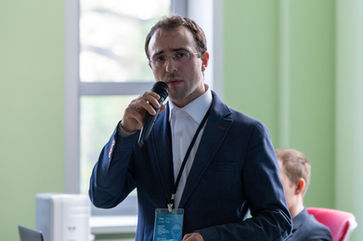 Loran Jacobs standing at a podium speaking on stage about AI startup acquisition during a business summit.