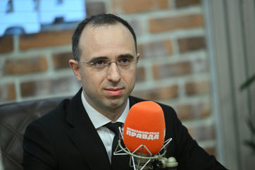 Loran Jacobs sitting at a broadcast microphone in a sound studio during an interview session.