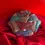Thumbnail: A luxury rose-shaped clutch encrusted with shimmering red, blue, and pink crystals, resting on a draped red satin fabric