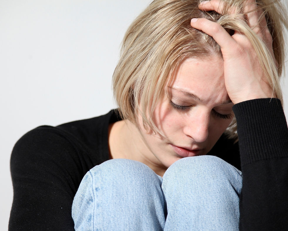 A woman with short, blonde hair, sitting with her head in her hands, and her knees pulled up to her chest.