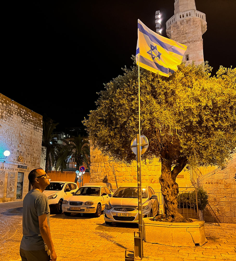 Bahar gazes at the Israeli flag in the historic Jewish Quarter of Jerusalem's Old Town at night, with the Tower of David Museum in the background.