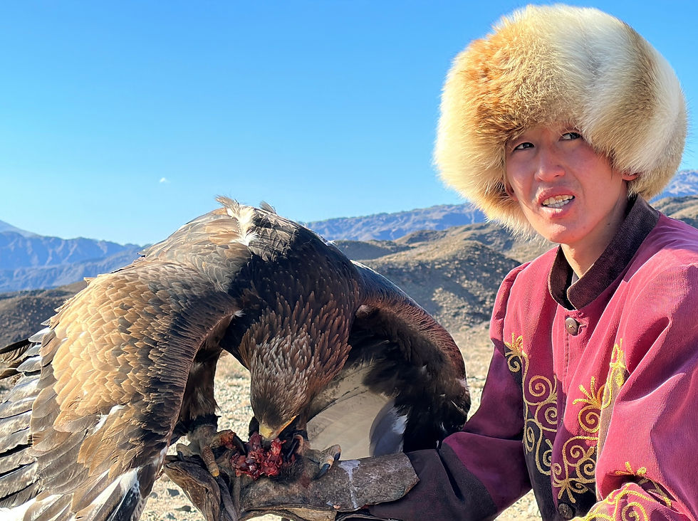 A skilled eagle master in traditional attire sits in the rugged landscape, showcasing the deep bond with his majestic bird of prey as it feeds.