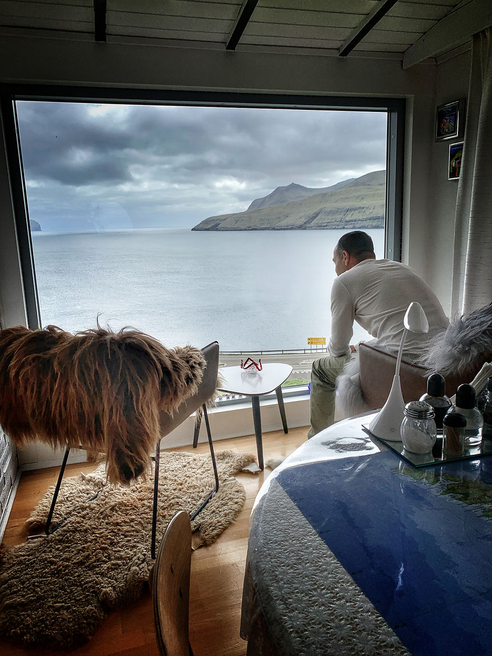 A serene moment as Bahar gazes out from a traditional house, enjoying the stunning landscape and water view through the window.
