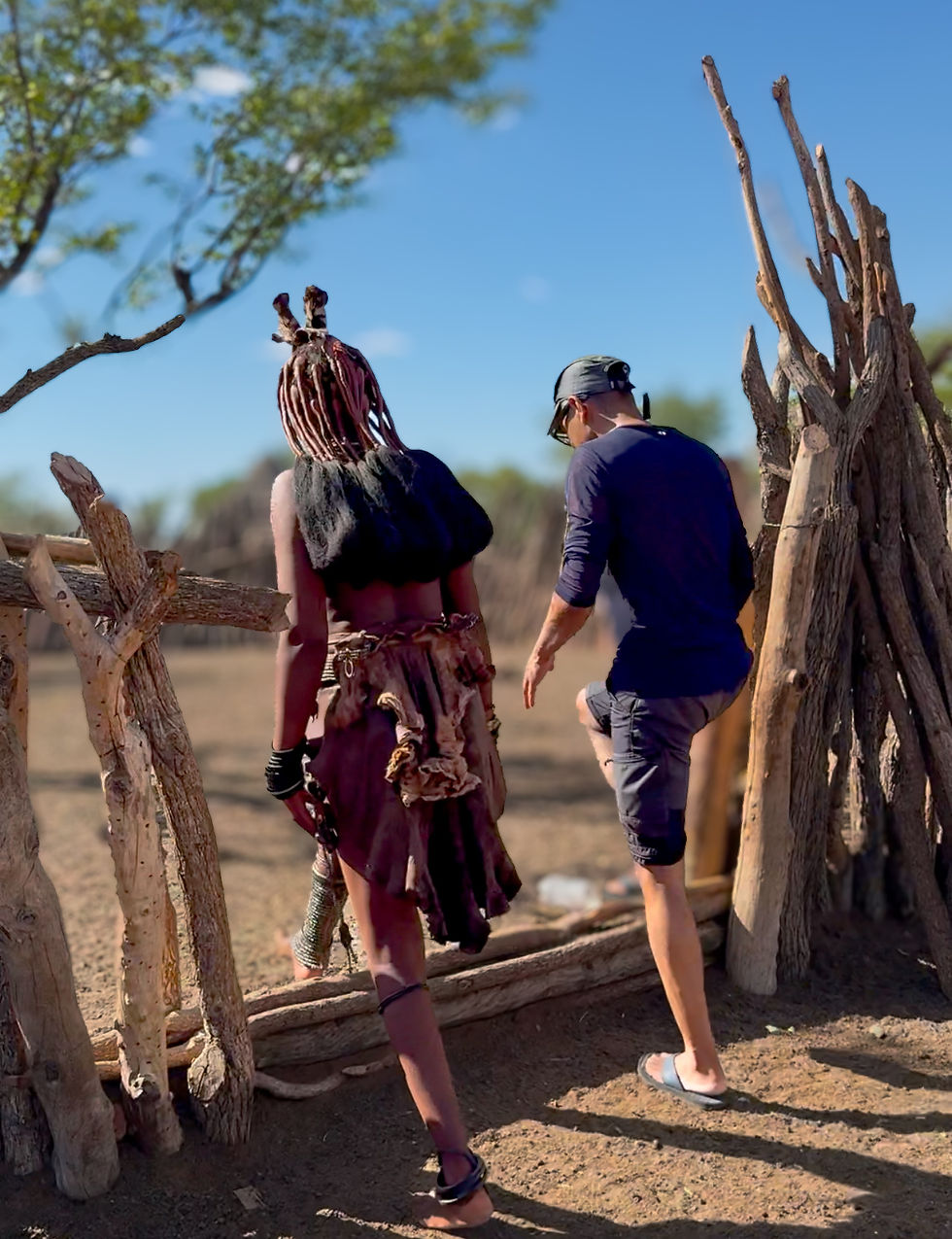 Bahar and a Himba woman walk through a traditional village entrance in Namibia, showcasing cultural diversity and rural life.