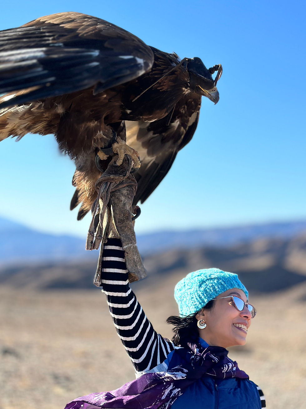 Sarmin joyfully holds the majestic eagle against a clear blue sky, capturing a moment of adventure and connection with nature.