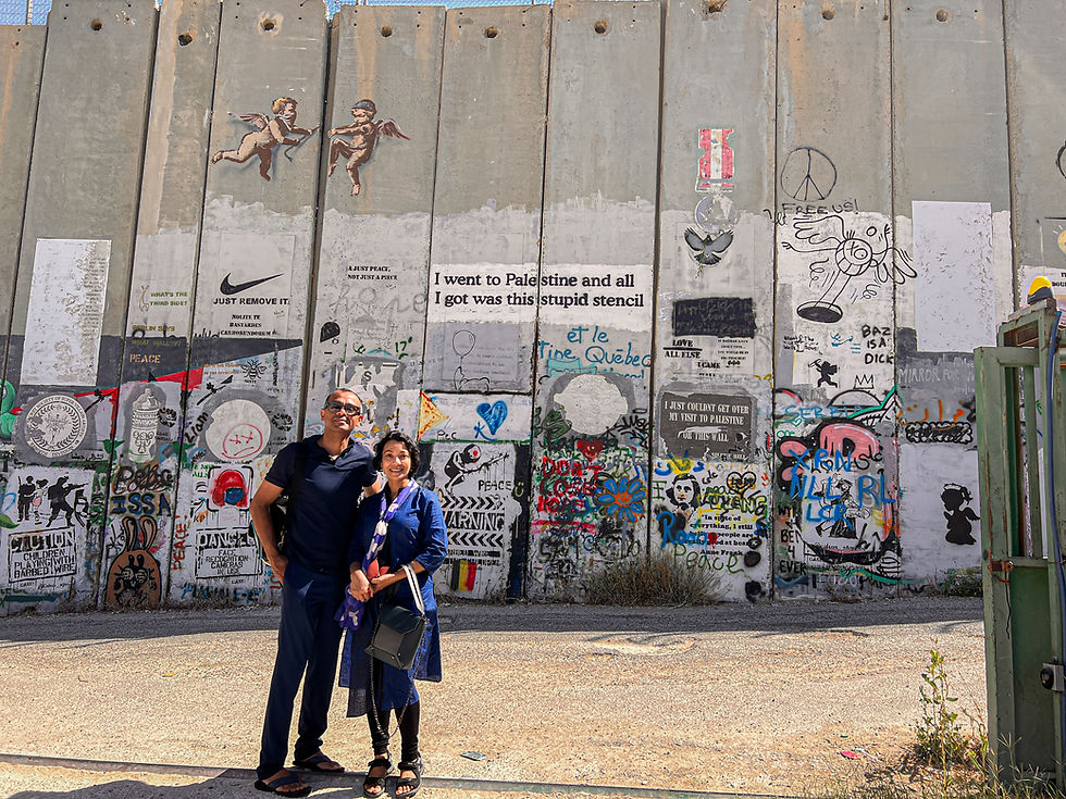 Sarmin & Bahar stand in front of the graffiti-covered separation wall in Bethlehem, showcasing vibrant street art and political statements about Palestine and Israel.