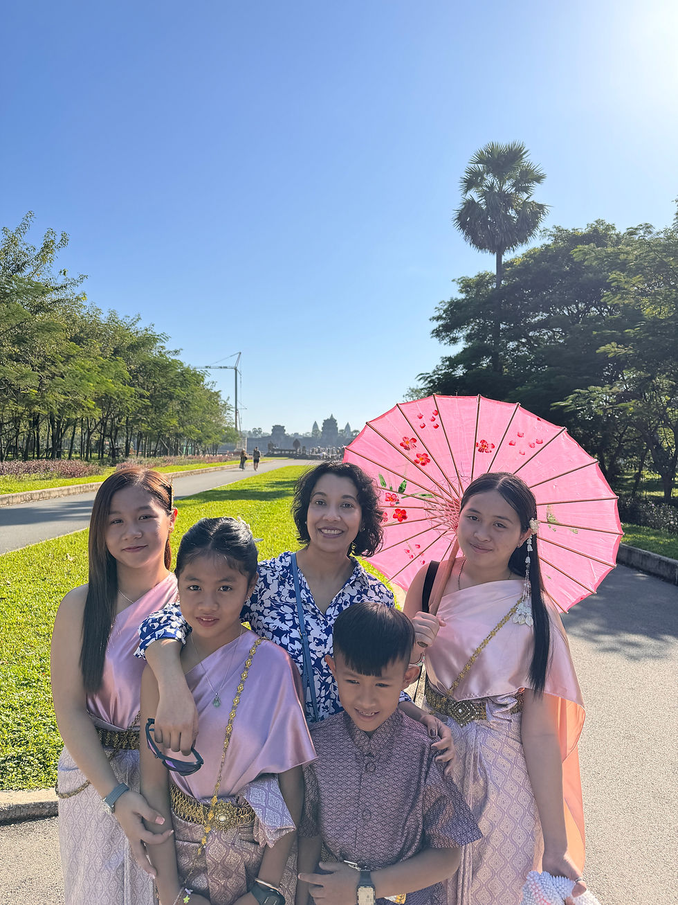 Sarmin enjoying a sunny day with local Cambodian children at Angkor, surrounded by lush greenery and holding a decorative pink parasol.