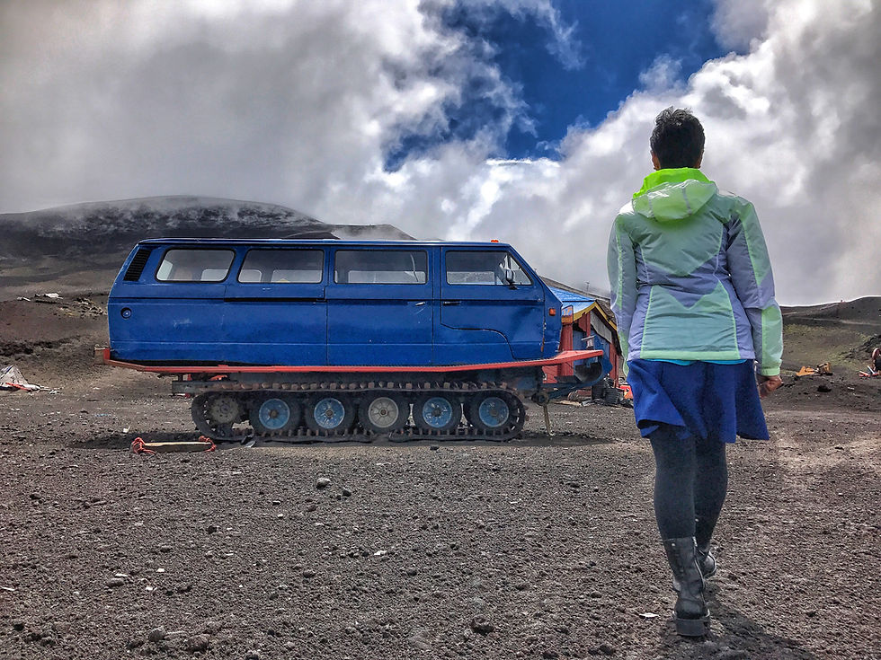 Sarmin approaches a unique tracked vehicle on the rugged terrain leading to Volcán Osorno, under a dramatic cloudy sky.