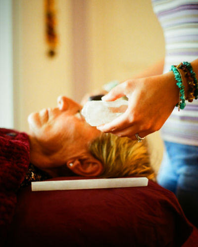 Emma carrying out an aura clearing on a client who is lay on her treatment bed with crystals around her head.