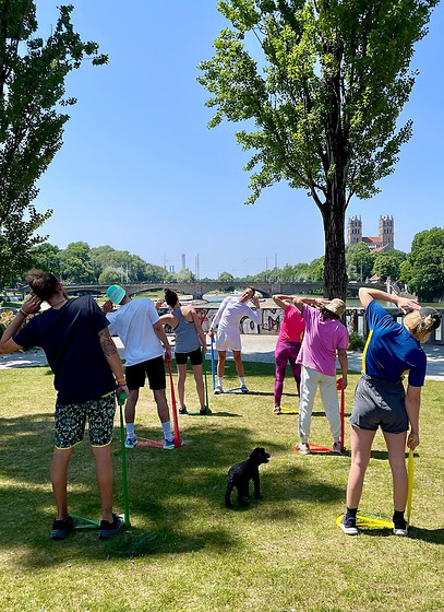 BandCamp Outdoor-Training in München an der Isar: Gruppe macht Mobilitätsübungen mit Widerstandsbändern im Park.