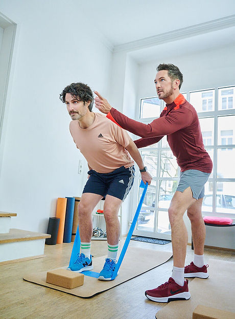 Personal Trainer in München zeigt einem Kunden eine Übung mit dem Widerstandsband für Kraft und Beweglichkeit.