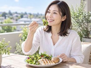 自宅のベランダのテーブルで、サラダとグリルチキン、パンを盛ったプレートからサラダをフォークで食べる女性