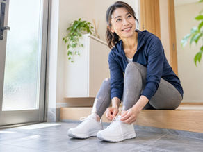 週1回のトレーニングに出かける前に、玄関で白いランニングシューズの靴ひもを結びながら笑顔を見せる女性