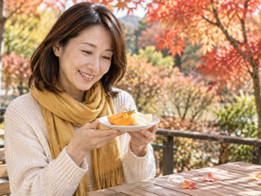 紅葉したカフェのテラス席で、柿と梨をのせた小皿を手に笑顔を見せる女性