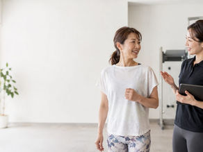 明るいトレーニングルームで、タブレットを持った女性トレーナーと白いTシャツの女性が笑顔で話している様子