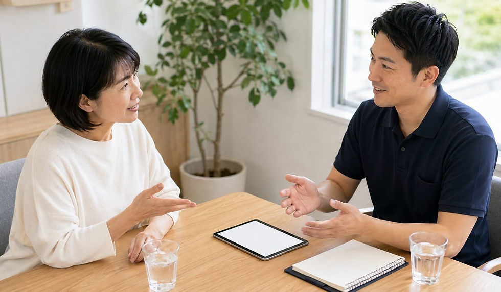 観葉植物のある明るい部屋で、女性と男性トレーナーがテーブルを挟んで話している様子