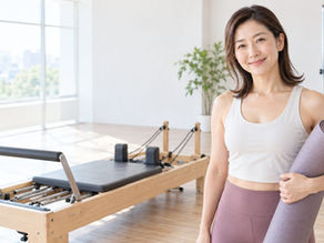 丸めたヨガマットを抱え、リフォーマーの横で微笑む女性