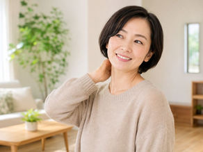 自宅のリビングで首の後ろに手を添え、軽く首をケアしている30代女性