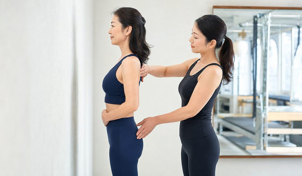 紺色のウェアの女性が横向きに立ち、背後のトレーナーが肩と腰に手を添えて姿勢を確認している
