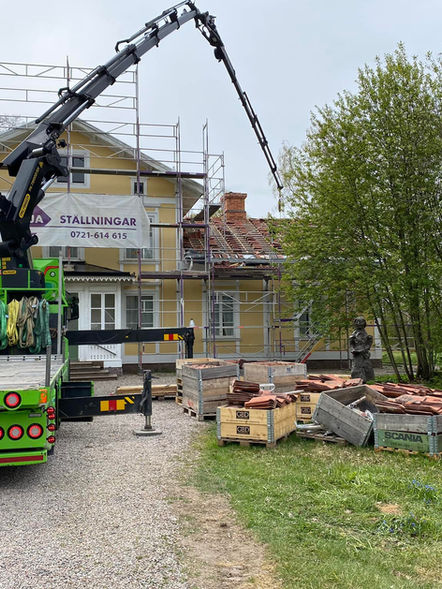 Fogelstad kvinnliga medborgarskola täckt i byggställningar. Taktegel i staplar på marken. En stor kran lyfter tegel upp på taket.