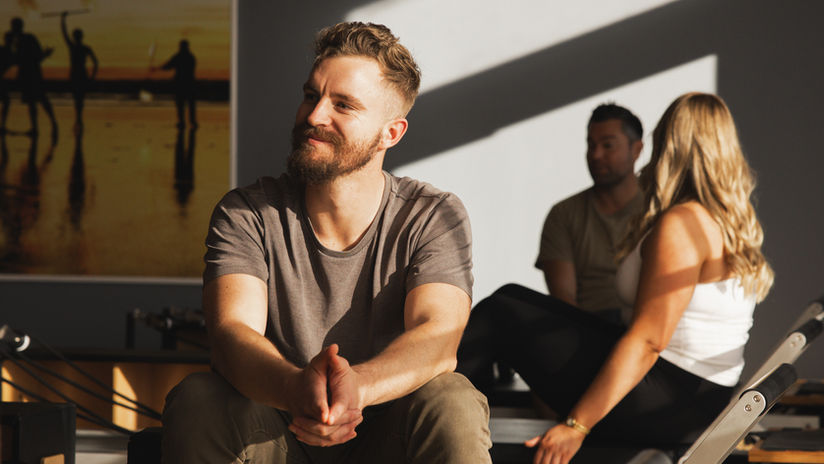 Members prepare for a Reformer Pilates session at ReDefined Gym in Papamoa, New Zealand, sitting on reformer machines in a bright, sunlit studio.
