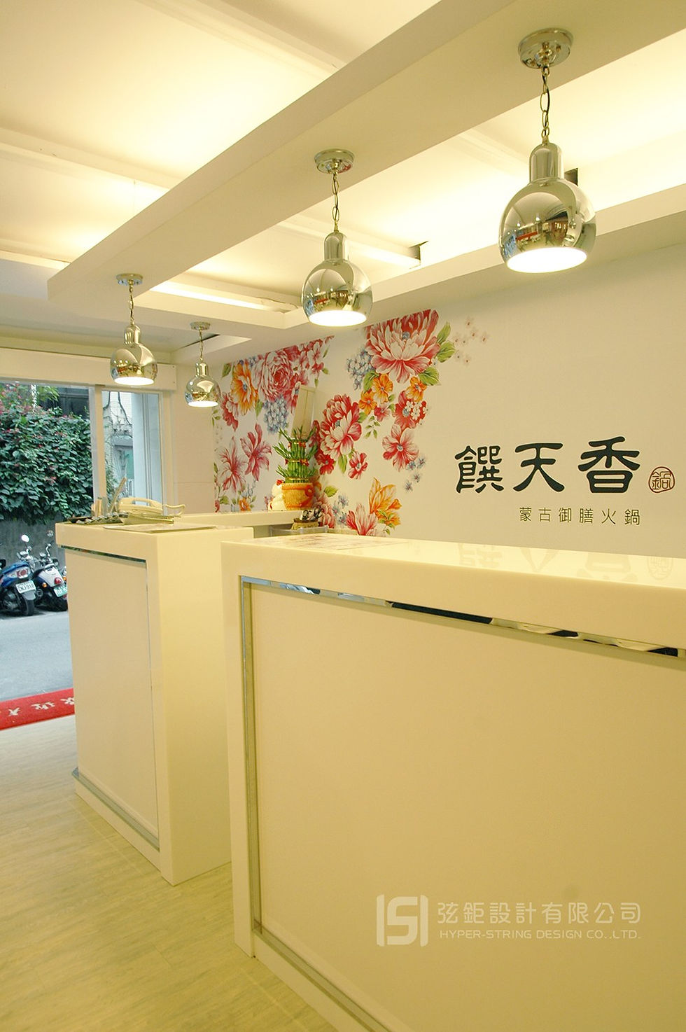 餐飲空間櫃檯設計，白色中島櫃體搭配花卉主題牆面與吊燈，營造明亮清新的品牌形象