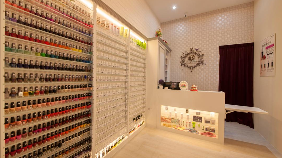 Modern spa reception with chandelier, white counter, cozy waiting area, and skincare product display.