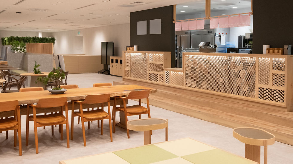 木製テーブルと椅子が並ぶ和風のモダンなカフェ。背景に格子細工のカウンターがあり、植物が置かれている。温かい雰囲気。
